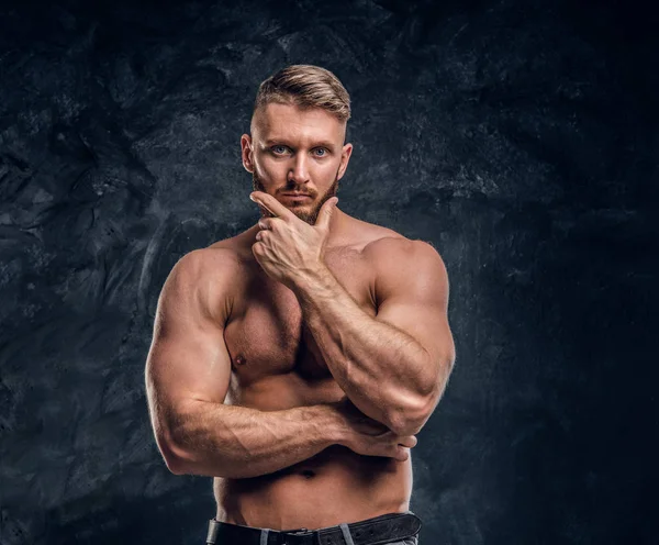 Bärtiger, hemdsloser Mann mit muskulösem Körper, der mit der Hand am Kinn posiert. Studiofoto vor dunklem Wandhintergrund — Stockfoto