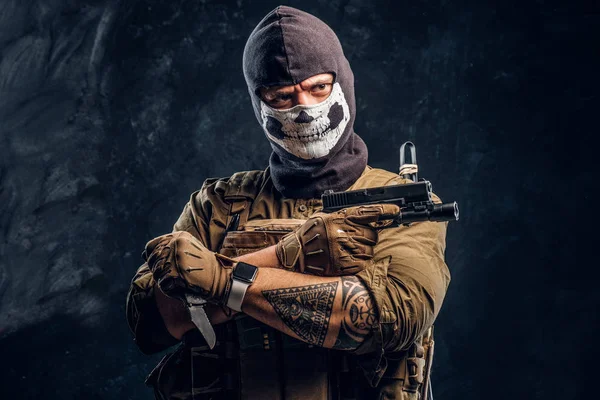 A terrorist in a military uniform and a skull balaclava holding a pistol and a knife and looks at the camera with a menacing look — Stock Photo, Image