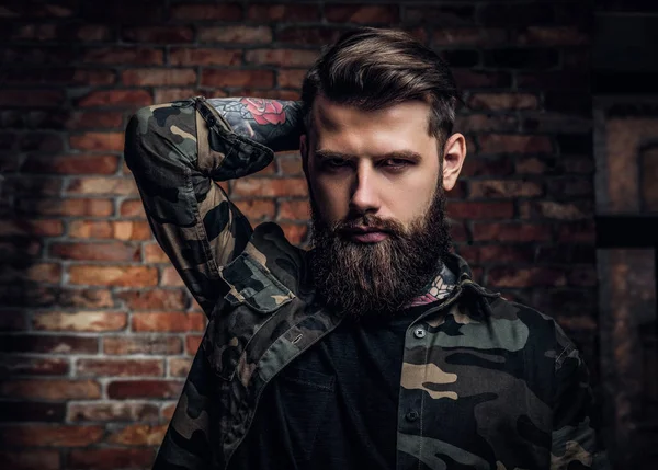 Retrato de um barbudo tatuado na camisa militar. Estúdio foto contra parede de tijolo — Fotografia de Stock