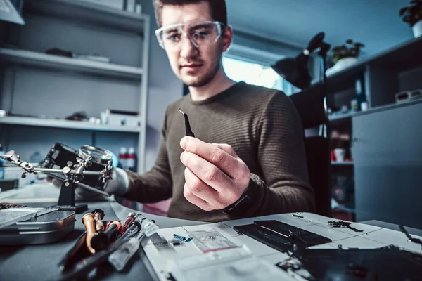 Elektronik teknisyeni kırık bir telefon tamir cımbızla tutan küçük cıvata yakından bakarak — Stok fotoğraf