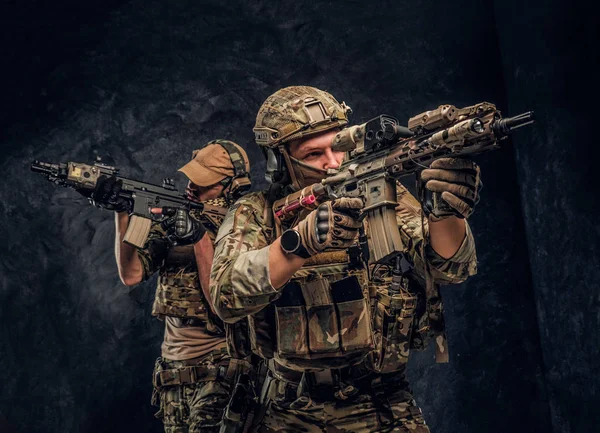 Zwei Soldaten einer Spezialeinheit in voller Schutzausrüstung halten Sturmgewehre in der Hand und zielen auf die Ziele. Studiofoto vor dunkel strukturierter Wand. — Stockfoto