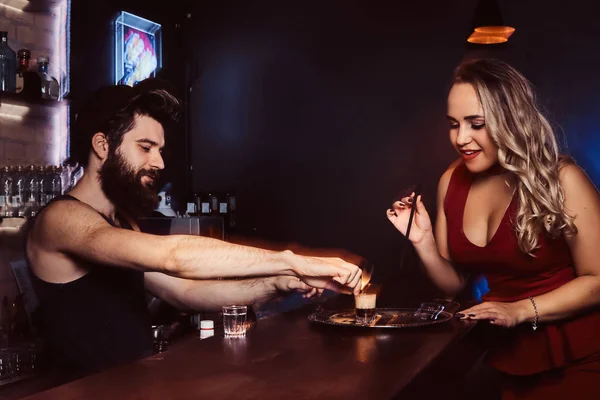 Una bella ragazza in abito rosso tiene in mano una cannuccia e aspetta che il barman faccia un cocktail — Foto Stock