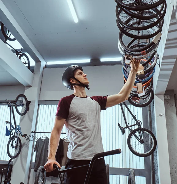 Joven en un casco de protección y la elección de neumáticos de bicicleta para su bicicleta en la tienda — Foto de Stock