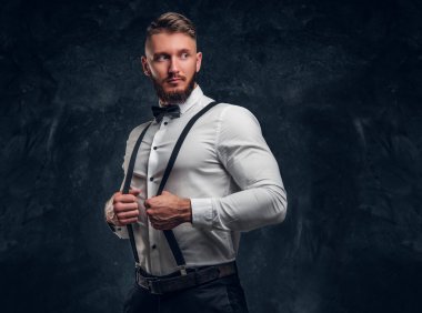 Şık genç adam papyon ve pantolon askısı ile gömlek giymiş. Studio fotoğraf karanlık duvar arka plan