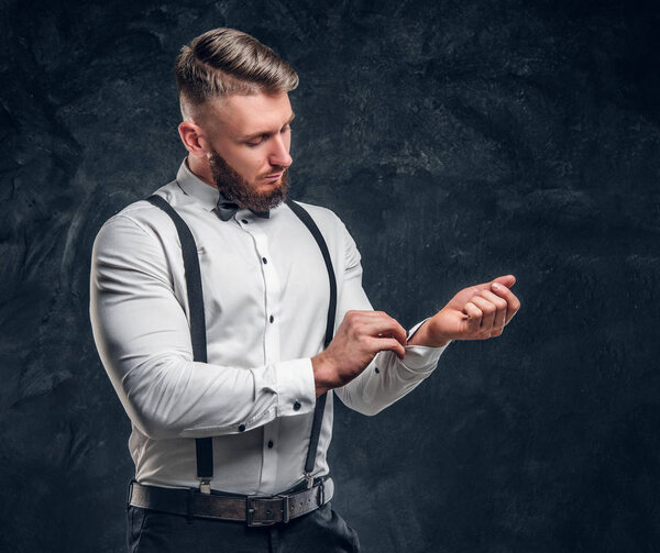 Stylishly dressed young man in shirt with bow tie and suspenders. Studio photo against dark wall background