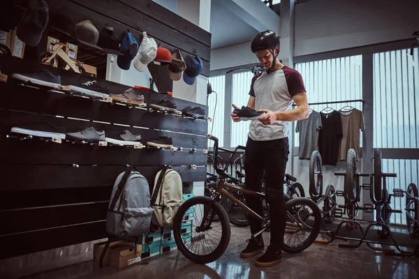 Młody mężczyzna stojący z jego rower, wybierając nowe trampki w sklepie. — Zdjęcie stockowe