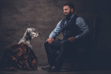 Onun iki safkan Setter köpek ile bir kanepede oturan zarif kıyafetlerle sakallı avcı.