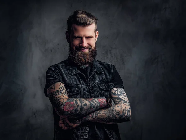 Egy stílusos szakállas srác portréja tetovált kezekkel. Fotóstúdió a sötét fal ellen — Stock Fotó
