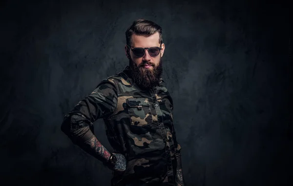 Retrato de un elegante barbudo con manos tatuadas en la camisa militar. Estudio foto contra la pared oscura — Foto de Stock