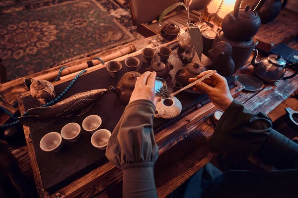 Mestre oriental vestindo um vestido cinza fazendo chá natural no quarto escuro com um interior de madeira. Tradição, saúde, harmonia. Cerimônia de chá chinês — Fotografia de Stock