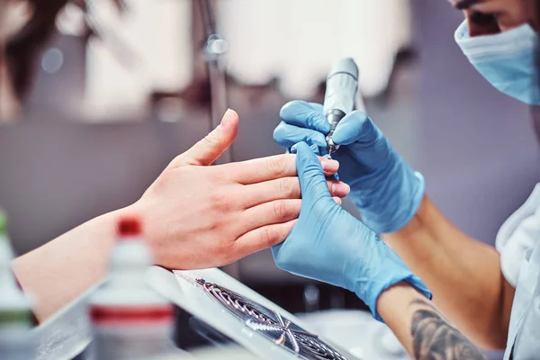 Mestre esteticista em luvas aplicando broca de unhas para aparar e remover cutículas. Manicura de hardware em um salão de beleza — Fotografia de Stock