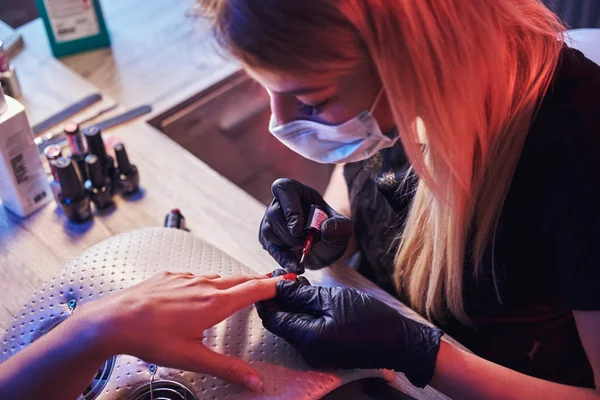 Top view of a beautician master applying polish on clients natural nails at the manicure table in the beauty salon.