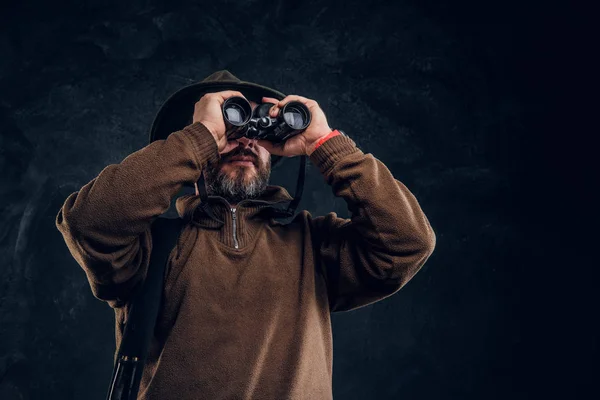 Hunter met Shotgun kijken door de verrekijker. Studio foto tegen donkere muur achtergrond — Stockfoto