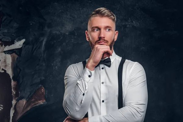 Nachdenkliche männliche Gedanken über etwas Wichtiges. stilvoll gekleideter junger Mann im Hemd mit Fliege und Hosenträgern posiert mit der Hand am Kinn. — Stockfoto