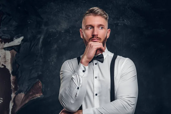 Homem pensativo a pensar em algo importante. Elegantemente vestido jovem em camisa com gravata borboleta e suspensórios posando com a mão no queixo . — Fotografia de Stock