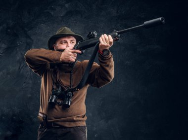 Hunter bir tüfek tutan ve hedef veya av hedefleyen. Koyu duvar arkaplanına karşı stüdyo fotoğrafı