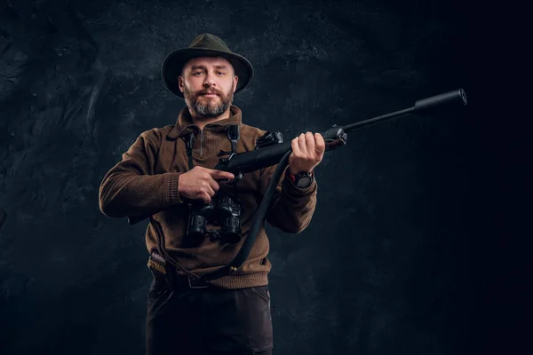 Cazador maduro con rifle y binoculares. Estudio foto contra fondo oscuro de la pared —  Fotos de Stock