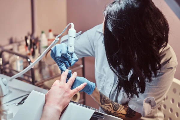 Kosmetikerin mit Handschuhen, die Nagelbohrer anwenden, um Nagelhaut zu schneiden und zu entfernen. Hardware-Maniküre im Schönheitssalon — Stockfoto