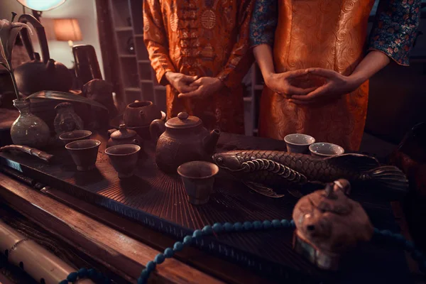 Китайська чайна церемонія. Пара чайної майстри стояли поруч з таблицею з набором для приготування чаю і аксесуарів в темній кімнаті з дерев'яним інтер'єром. — стокове фото