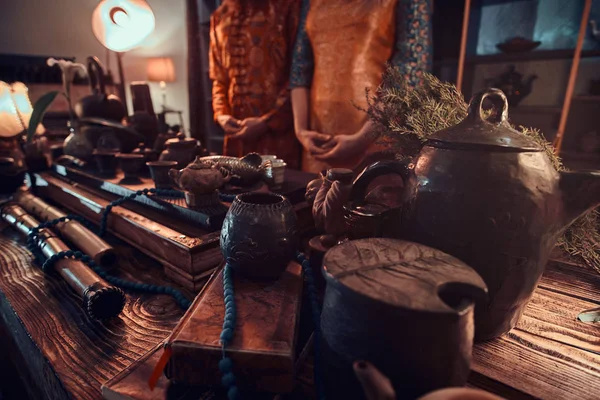 Cérémonie du thé chinois. Couple de maîtres du thé debout à côté d'une table avec un ensemble pour faire du thé et des accessoires dans la pièce sombre avec un intérieur en bois . — Photo
