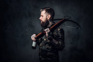 Askeri gömlek bir zanaat bira ve bir ortaçağ yay tutan şık sakallı hipster adam. Koyu duvara karşı stüdyo fotoğrafı