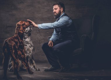 Onun iki safkan Setter köpek ile bir kanepede oturan zarif kıyafetlerle sakallı avcı.