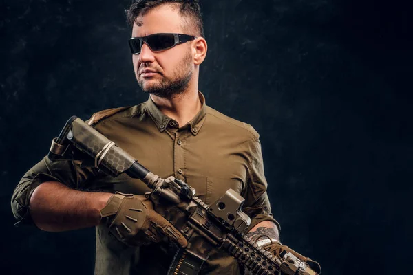 Retrato de um homem elegante usando óculos de sol camisa segurando rifle assalto e olhando para o lado . — Fotografia de Stock