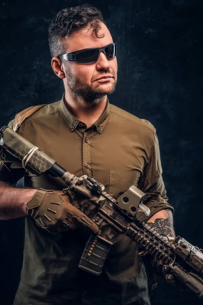 Portrait of a stylish man wearing shirt sunglasses holding assault rifle and looking sideways.