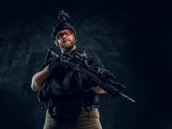 Soldado das forças especiais usando armadura e capacete com visão noturna segurando um rifle de assalto. Foto do estúdio contra uma parede de textura escura — Fotografia de Stock