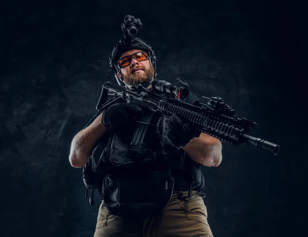 Soldado de las fuerzas especiales con chaleco antibalas y casco con visión nocturna sosteniendo un rifle de asalto. Foto del estudio contra una pared de textura oscura —  Fotos de Stock