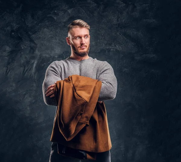 Belleza para hombre, moda de temporada. Retrato de un hombre elegante sosteniendo su abrigo de temporada. Foto del estudio contra un fondo de pared oscuro — Foto de Stock