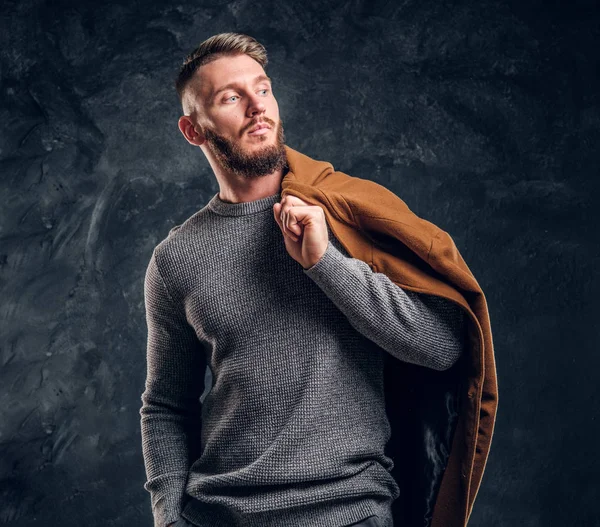 Beleza masculina, moda sazonal. Homem elegante posando com casaco de estação demi em um ombro. Foto do estúdio contra um fundo de parede escura — Fotografia de Stock