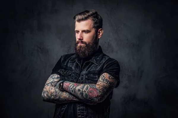 Portrait of a stylish bearded guy with tattooed hands. Studio photo against dark wall — Stock Photo, Image