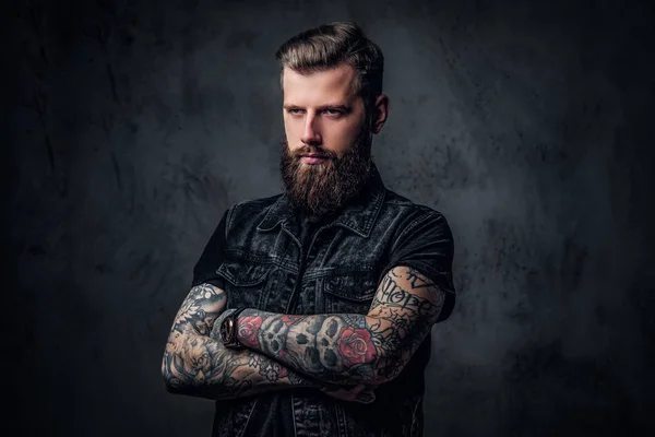 Portrait of a stylish bearded guy with tattooed hands. Studio photo against dark wall — Stock Photo, Image