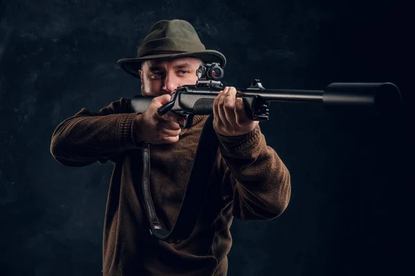 Hunter sostiene un rifle y apunta a su objetivo o presa. Estudio foto contra fondo oscuro de la pared —  Fotos de Stock