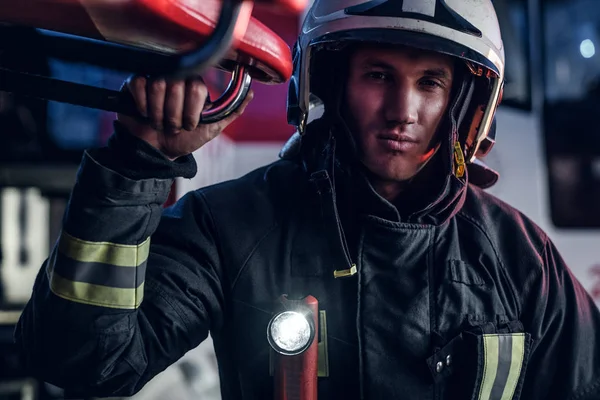 Portrait of a handsome fireman wearing a protective uniform with flashlight included standing in a fire station garage — Stock Photo, Image