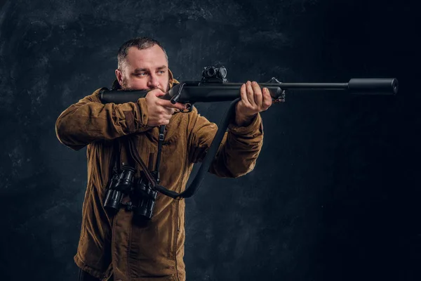 Hunter sostiene un rifle y apunta a su objetivo o presa. Foto del estudio contra un fondo de pared oscuro — Foto de Stock