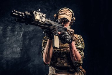 Karanlık bir duvara yakın çekim studio fotoğraf. Elit birimi, Özel Kuvvetler asker bir saldırı tüfeği bir lazer görme ve amaçlar ile hedef tutan kamuflaj üniformalı