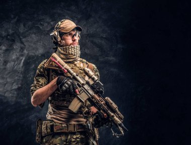 Asker kamuflaj bir saldırı tüfeği tutan tek tip içinde tam donanımlı. Karanlık bir duvara Studio fotoğraf