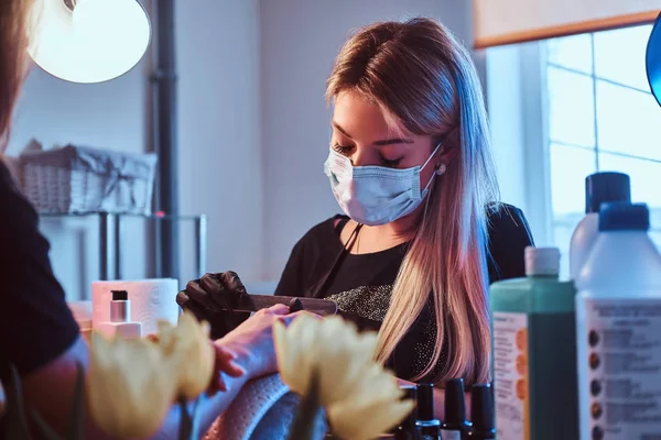 Atractivo maestro de manicura femenina está trabajando con las uñas del cliente en el salón de belleza. Hay flores en la mesa. . —  Fotos de Stock