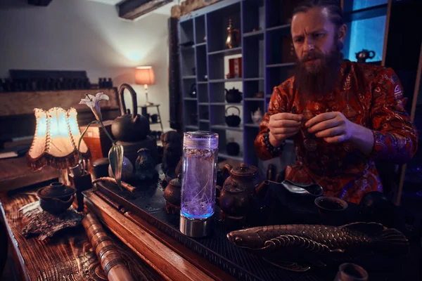 Майстер чаю в кімоно робить натуральний чай в темній кімнаті з дерев'яним інтер'єром, спостерігаючи за чайним листям під час заварювання — стокове фото
