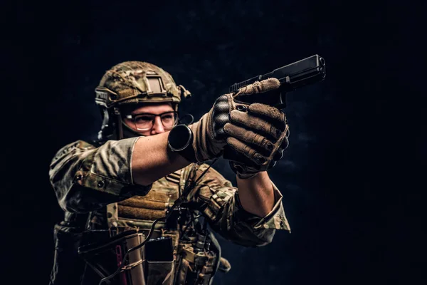Foto de estúdio contra uma parede de textura escura. A unidade de elite, o soldado das forças especiais em uniforme de camuflagem com uma pistola e aponta para o alvo — Fotografia de Stock