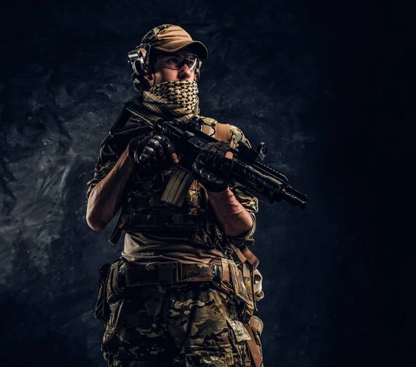 Soldado totalmente equipado em uniforme de camuflagem com uma espingarda de assalto. Foto de estúdio contra uma parede escura — Fotografia de Stock