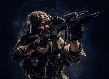 Karanlık bir duvara yakın çekim studio fotoğraf. Elit birimi, Özel Kuvvetler asker bir saldırı tüfeği bir lazer görme ve amaçlar ile hedef tutan kamuflaj üniformalı