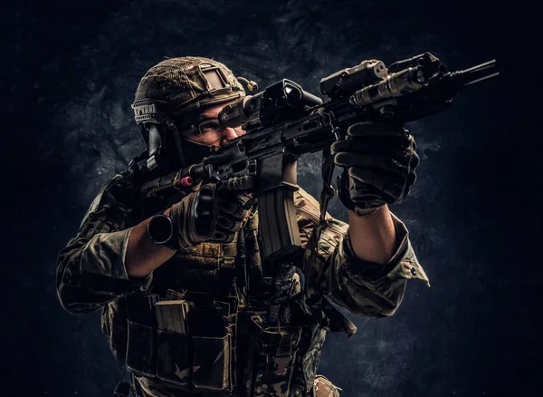 Närbild foto mot en mörk vägg i studion. Elitenheten, specialstyrkor soldat i kamouflage uniform håller en automatkarbin med ett lasersikte och syftar på targe — Stockfoto