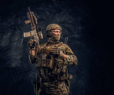 Asker kamuflaj bir saldırı tüfeği tutan tek tip içinde tam donanımlı. Karanlık bir duvara Studio fotoğraf