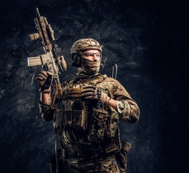 Asker kamuflaj bir saldırı tüfeği tutan tek tip içinde tam donanımlı. Karanlık bir duvara Studio fotoğraf