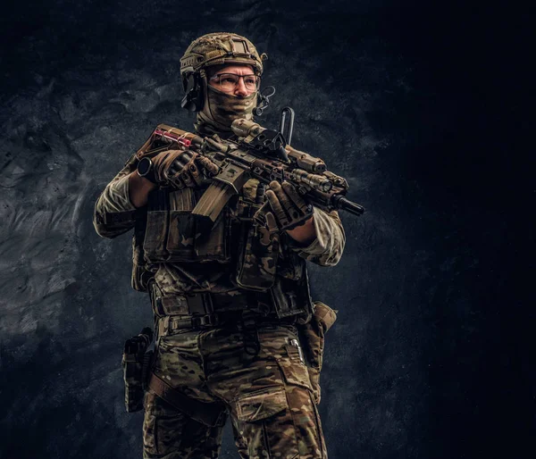 Asker kamuflaj bir saldırı tüfeği tutan tek tip içinde tam donanımlı. Karanlık bir duvara Studio fotoğraf