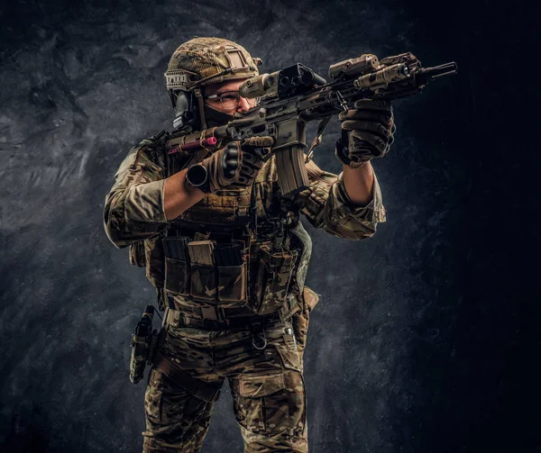 De elite eenheid, speciale troepen soldaat in camouflage uniform houdt een aanvalsgeweer met een laser zicht en doelstellingen op de doelgroep. Studio foto tegen een donkere muur — Stockfoto
