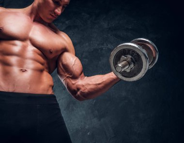 Çıplak kas gövdesi ile güçlü erkek dumbbell ile execise yapar ve onun büyük Muscules gösterir. Karanlık arka plan.